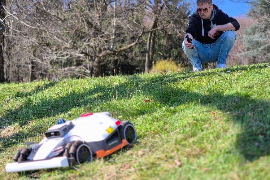 Mammotion LUBA 3 AWD Mähroboter fährt eigenständig einen steilen Hang hinauf. Smart Home Fox Tester beobachtet das Fahrverhalten auf nassem Untergrund. 